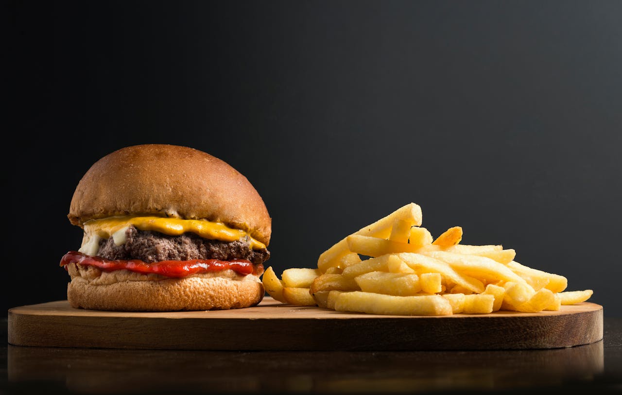 creative Appetizing burger with meat patty ketchup and cheese placed on wooden table with crispy french fries against black background
