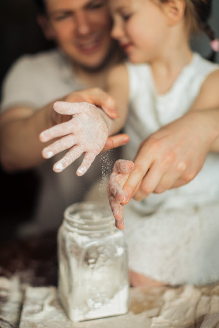 creative-02 Happy crop cute girl with pigtail and blurred father shaking off flour from hands while making dough