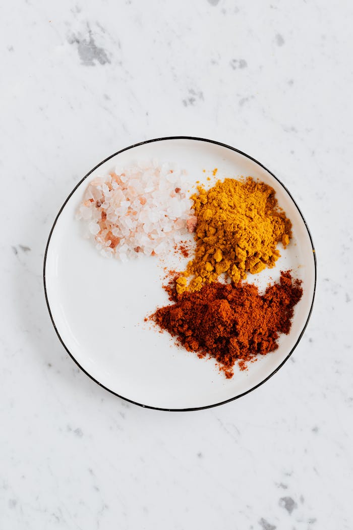 brand-03 Top view of different powdered spices of curcuma and chili with pink salt in metal bowl on white marble surface
